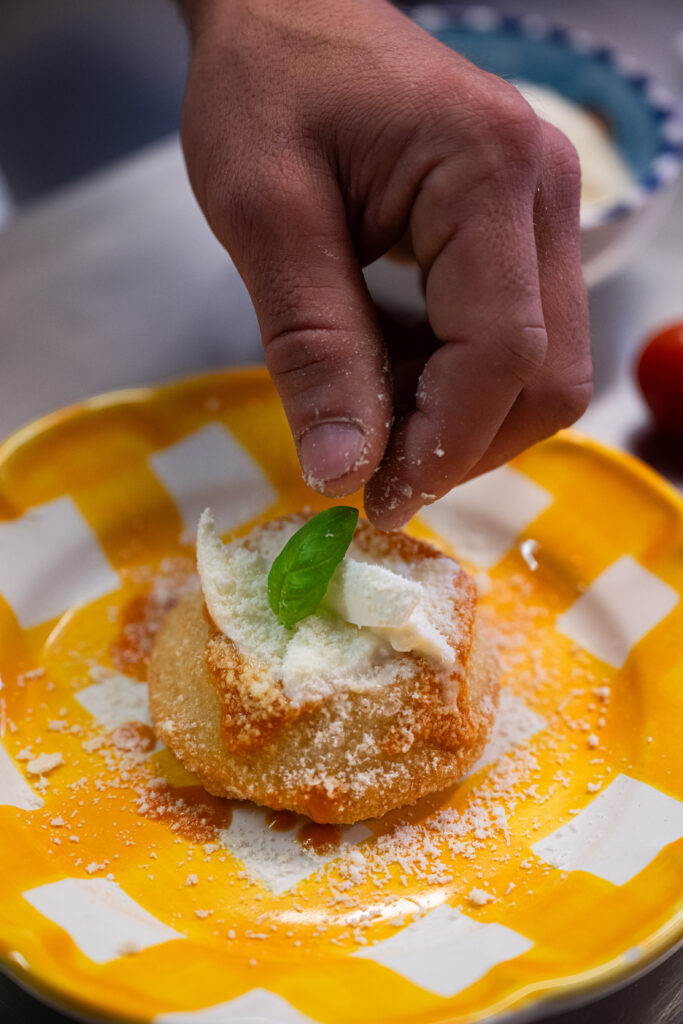 Hand adding a basil leaf to a golden fried dish with cheese on a yellow checked plate