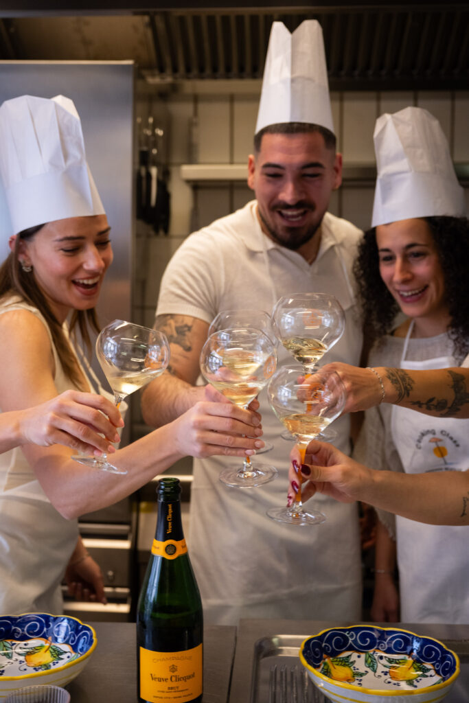 Three guests in aprons toasting with white wine next to a bottle of Veuve Clicquot