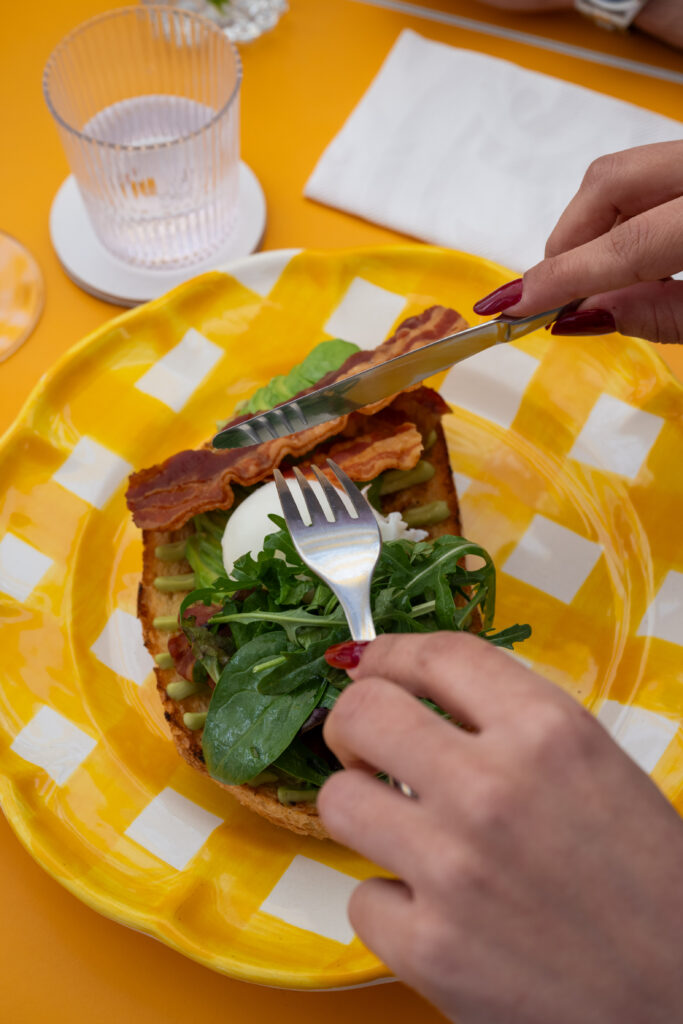 Hands cutting a savory toast with rocket on a yellow and white checked plate