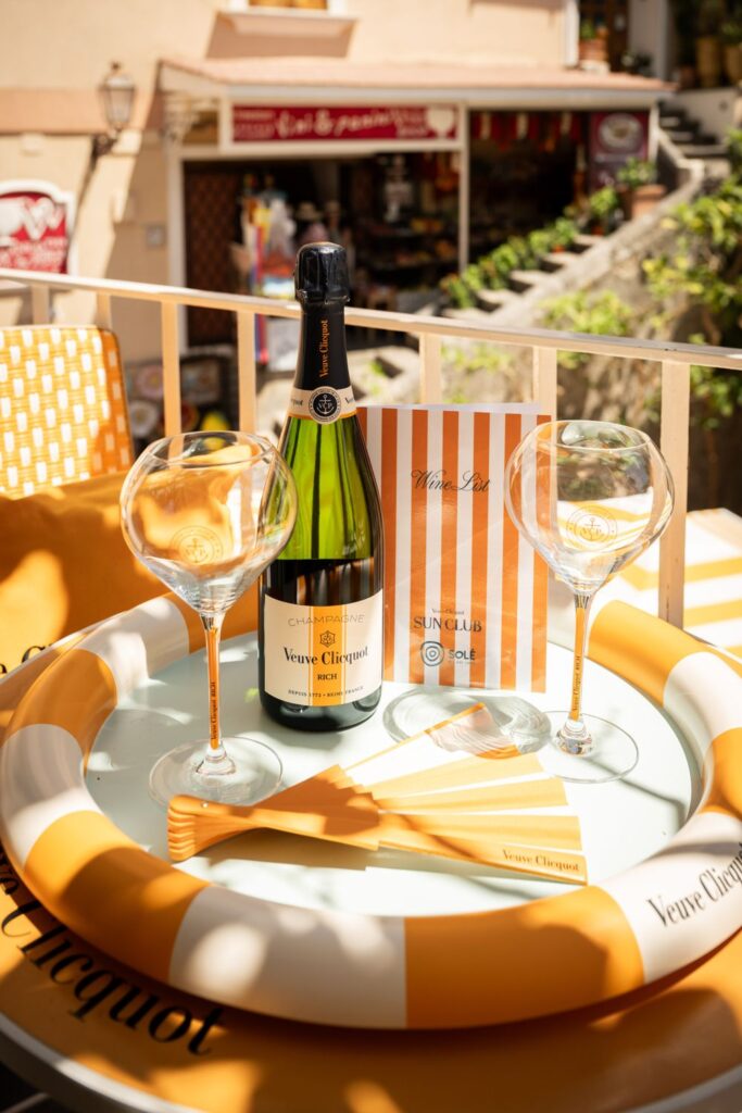 Veuve Clicquot bottle, two glasses and the Sun Club wine list on a striped tray