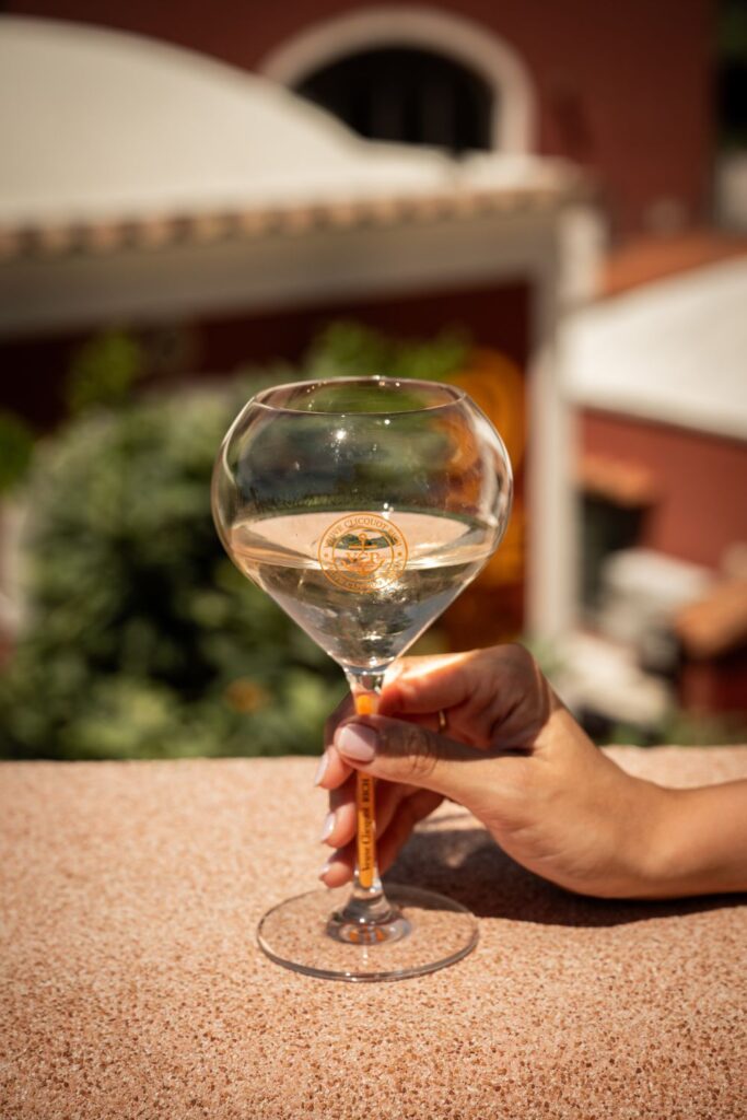 A hand holding a Veuve Clicquot Rich glass in the sun